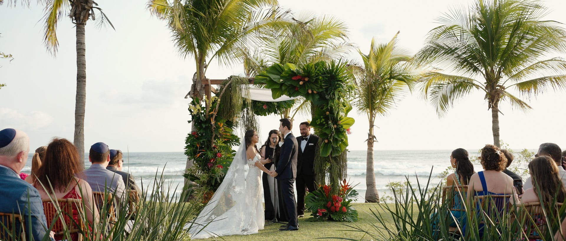 Becca and Jared exchanging vows under a floral arch during their beachside wedding ceremony at Hacienda Pinilla.