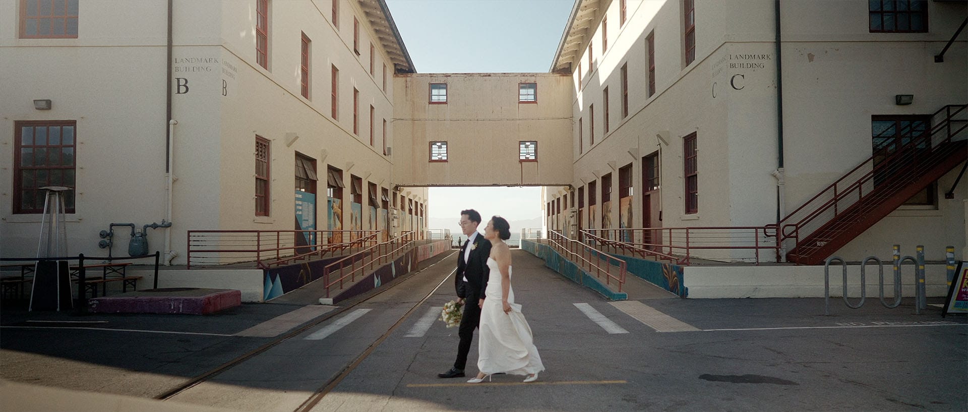 Bride and groom walk between historic buildings.